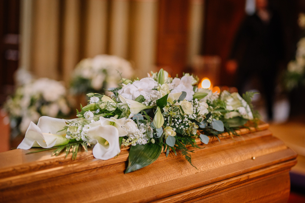 En kista dekorerad med många blommor och ljus i en vacker kyrka vid en begravnings ceremoni